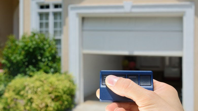 Hand holding remote control garage door opener with garage door in background.