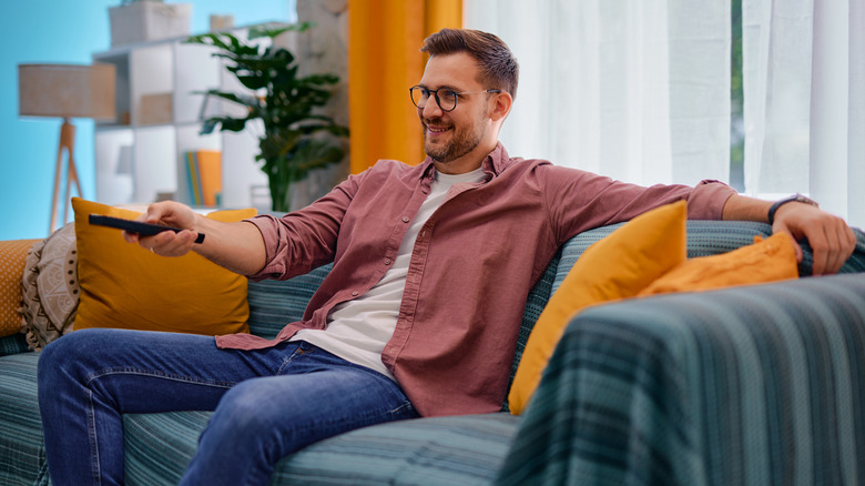 Man watching television in bright room pointing remote off screen