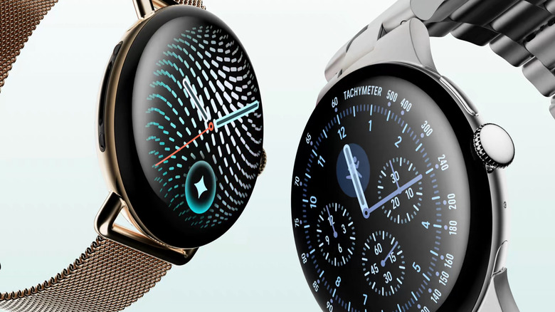 Two Google Pixel 5 smartwatches with metallic cases and digital watch faces displayed against a pale background.