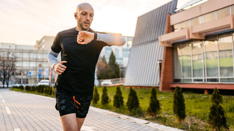 A man checks his smartwatch while running outdoors near a modern building.