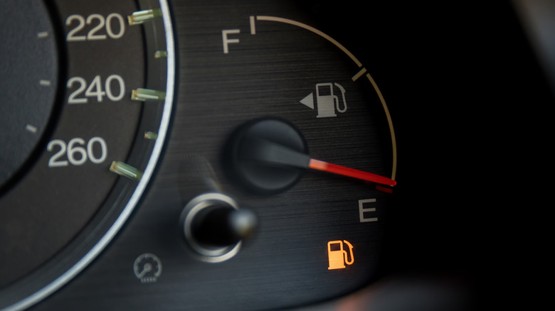 Close-up of a fuel gauge on a car dash showing close to empty with the fuel light lit