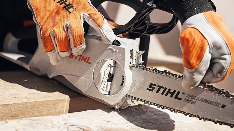 A person holding a Stihl chainsaw with gloves.