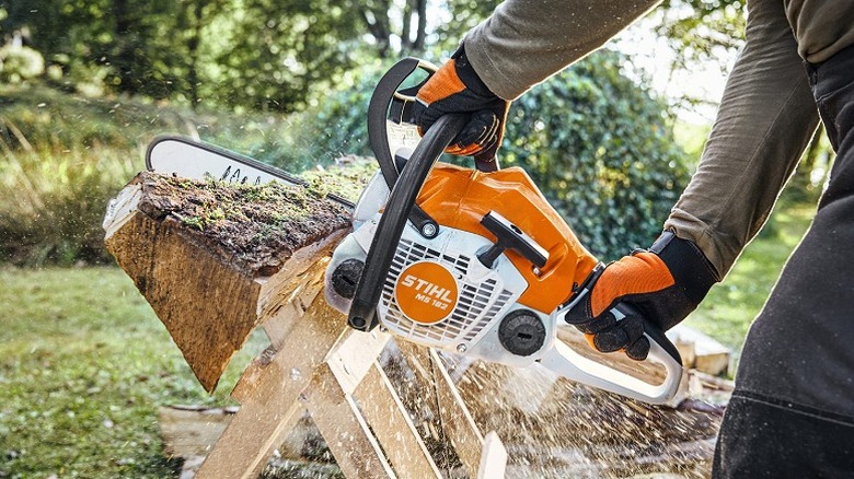 A person with gloves cutting wood with the MS 162.