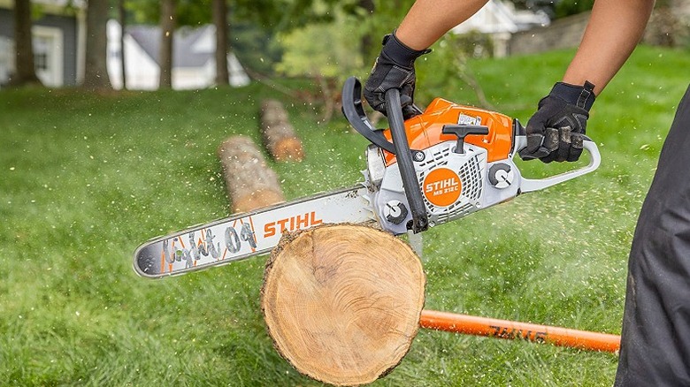 A person with gloves using Stihl MS 212 chainsaw to cut a log.
