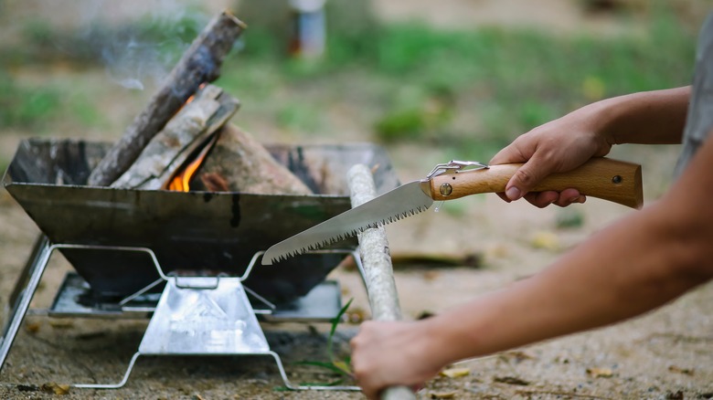 folding saw cutting firewood by campfire 