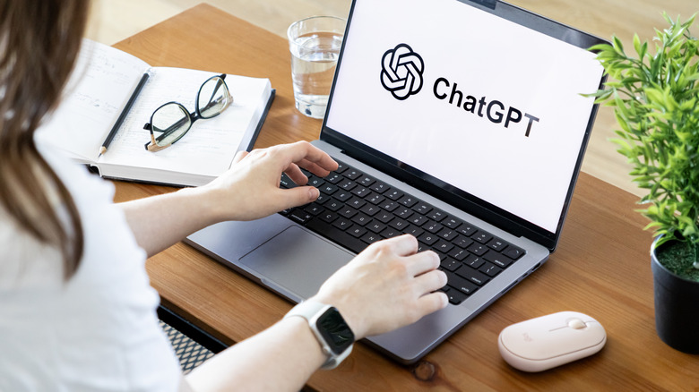 Woman sitting at a desk with a laptop displaying the ChatGPT logo.