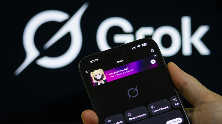 Close up of a mans hand holding a smartphone running Grok, with the Grok logo prominent in the background