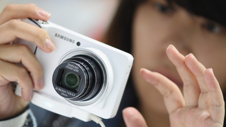 A woman holding a white Samsung digital camera