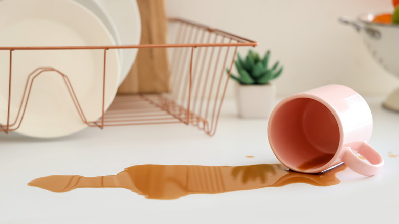 Pink mug that has spilled brown liquid on a white countertop