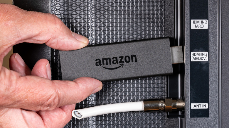 An Amazon Fire TV Stick being inserted into the HDMI port of a television