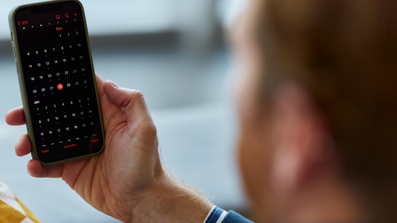 A man holding up an iPhone with the Calendar app on the screen