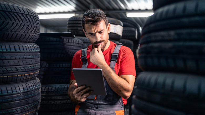 A worker appearing to look on a iPad with tires behind him