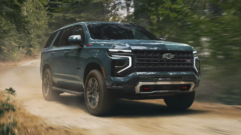 Teal 2026 Chevrolet Tahoe driving on a forested dirt road