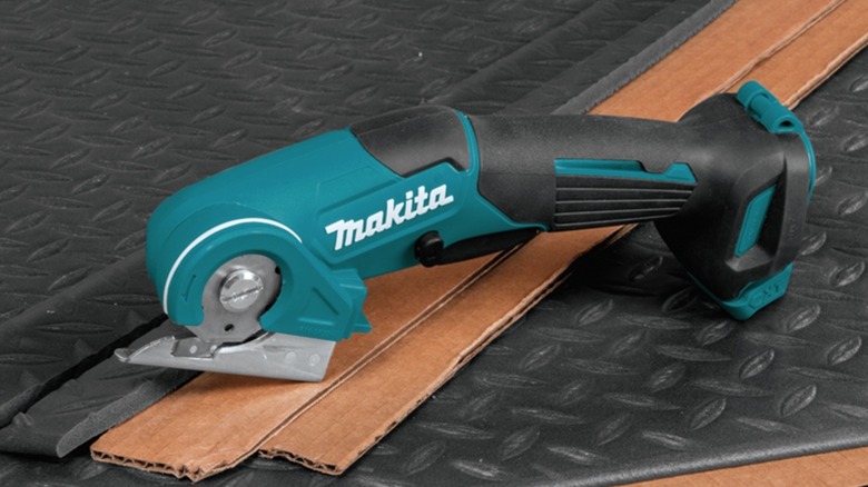 A Makita 12V multi-cutter laid atop cut sheets of cardboard and rubber.