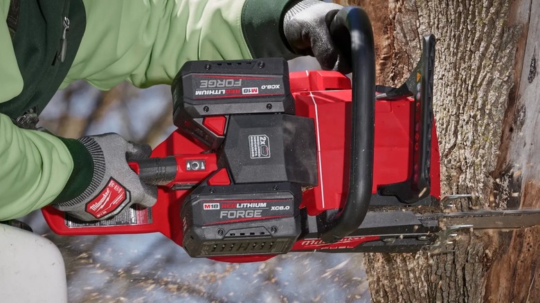 A person using a Milwaukee M18 chainsaw on a tree.