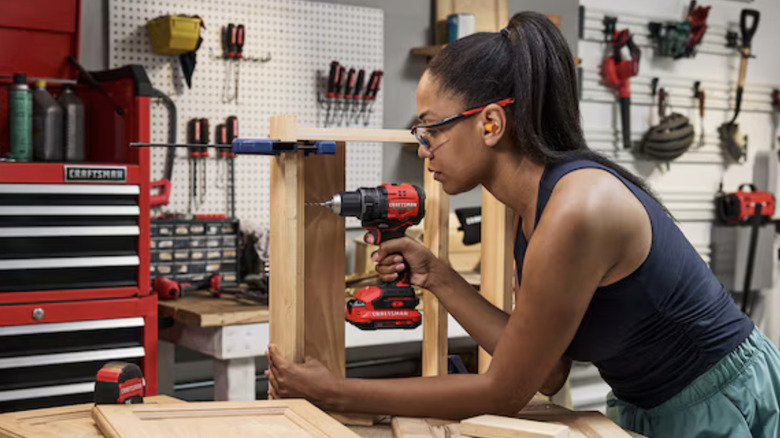 A woman in a workshop using a Craftsman cordless drill on a woodworking project