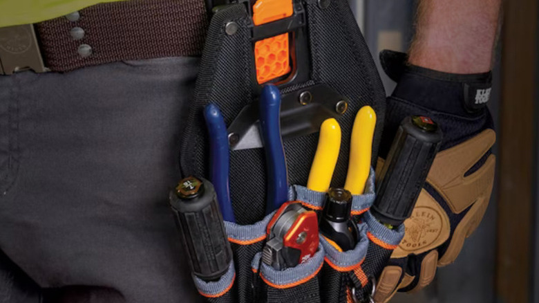 A close-up of the Klein Tools 6-Pocket Tool Pouch attached to a man's belt and holding tools