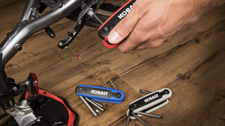 A close-up of the Kobalt 25-piece Hex Key Set with a hand using one set to repair a bicycle chain