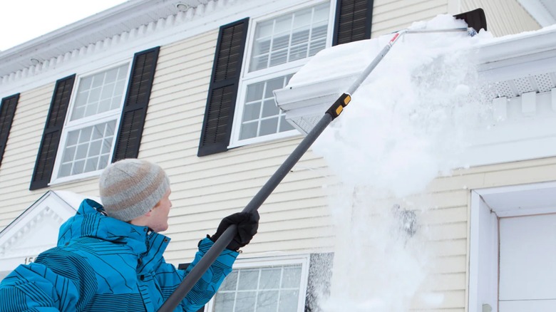 A person raking snow off of their roof.