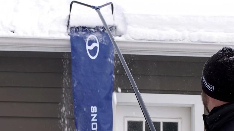 A person using a Snow Joe roof rake on a house.