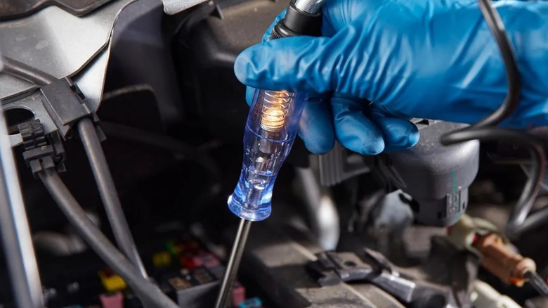 A person using a Cen-Tech test light to inspect fuses