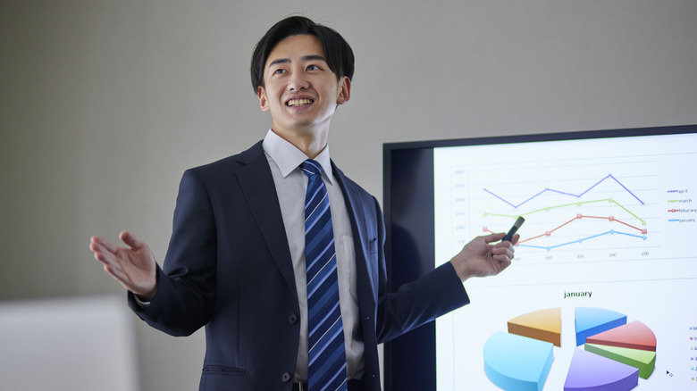 A person standing in front of a slide presentation, remote in hand.