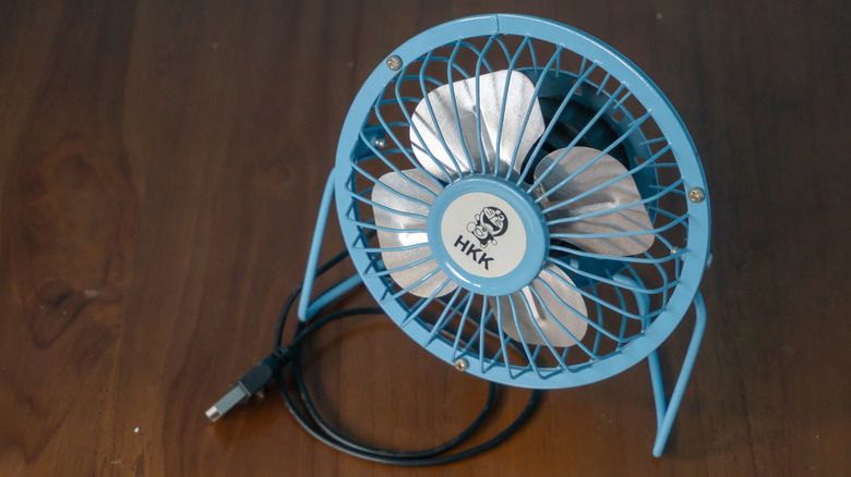 Light blue fan with USB cord on wooden floor