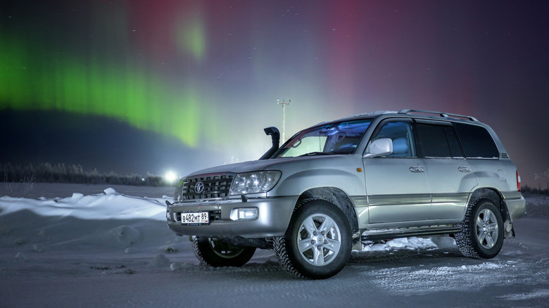 An older 2000s Toyota Land Cruiser parked at night, with the Northern Lights glowing in the background.