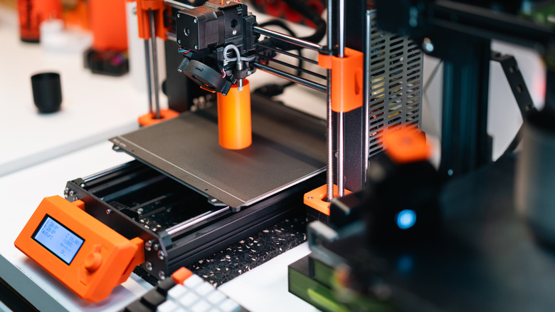 A 3D printer being used to print a plastic orange cylinder