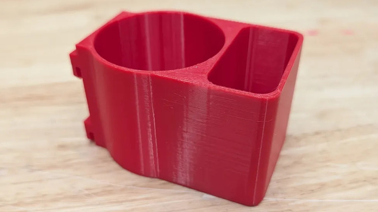 A 3D-printed glue holder for Home Depot's red rack shelving unit, resting on a wood surface