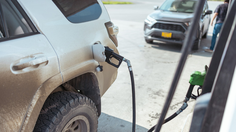 A Toyota 4Runner covered in dirt being filled up at a gas station, close up of the fuel door