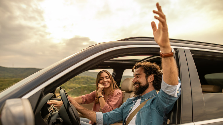 Man driving with hand up comfortably in car with woman next to him