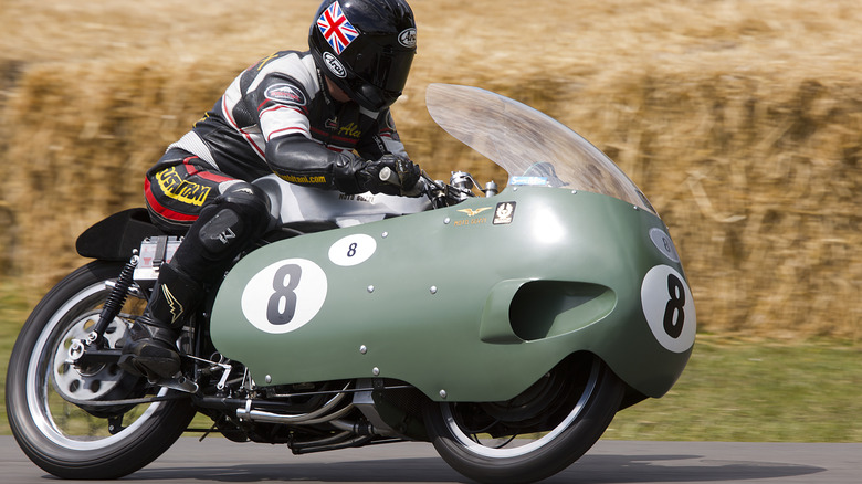 A green 1955 Moto Guzzi V8, or Otto Cilindri motorbike being ridden by a rider in full kit and helmet around a track.