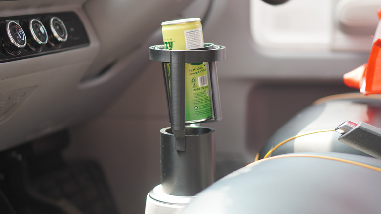A beverage can placed inside a 3D-printed gimbal cup holder, inside a car.