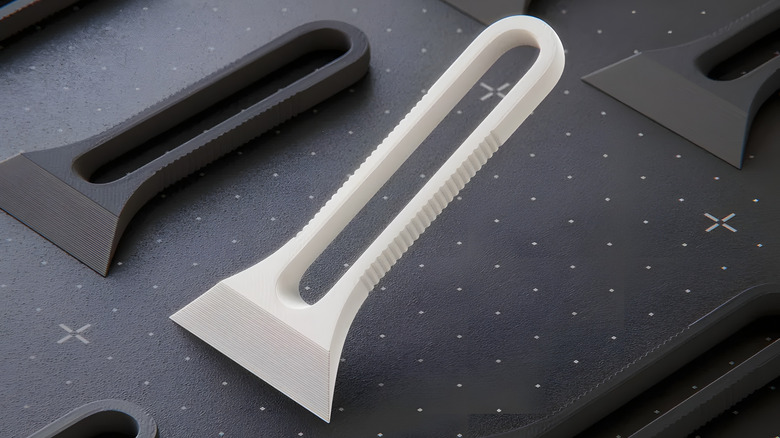 A 3D printed bed scraper in multiple colors lying on a 3D printer bed