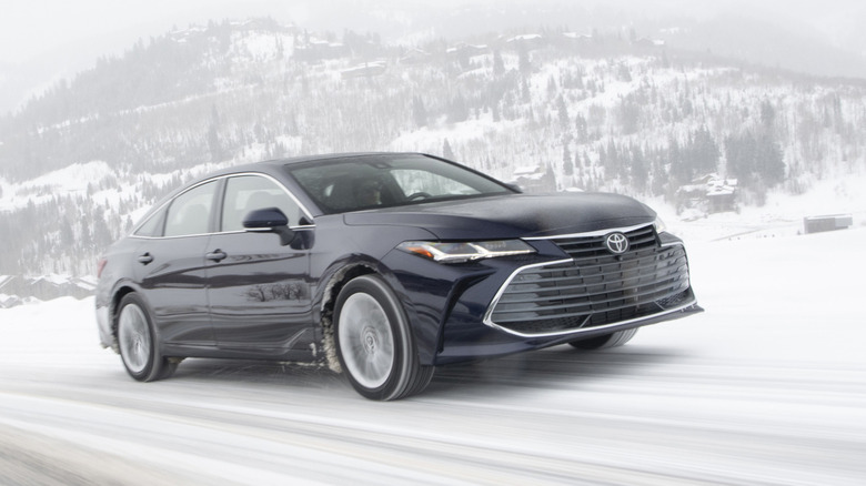 Front 3/4 view of black Toyota Avalon Hybrid driving on snowy mountain road.