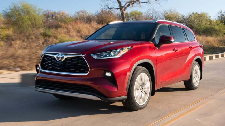 Front 3/4 view of red Toyota Highlander Hybrid driving on rural highway.