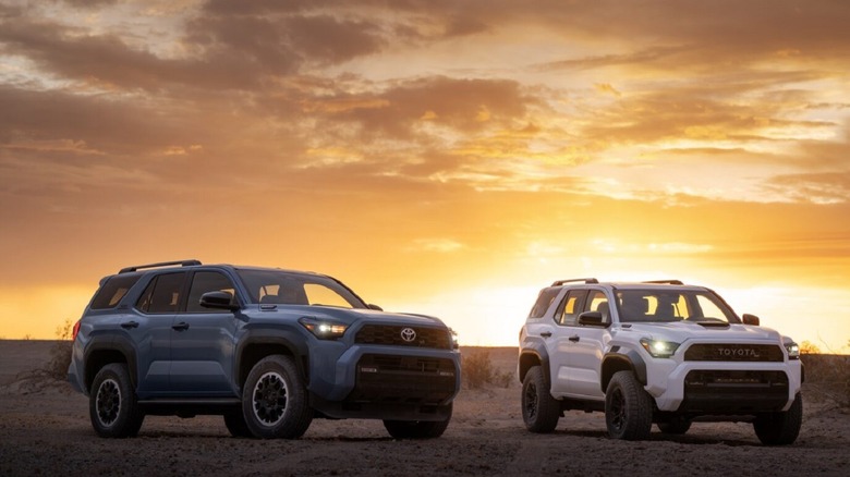 A pair of four-cylinder Toyota 4Runners parked on the dirt in front of a sunset