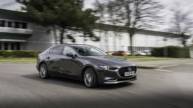 A gray Mazda3 Sedan on the move in an urban area, front 3/4 view, UK plates