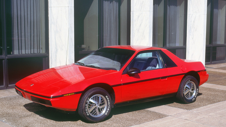 Red 1983 Pontiac Fiero parked in front of a building.