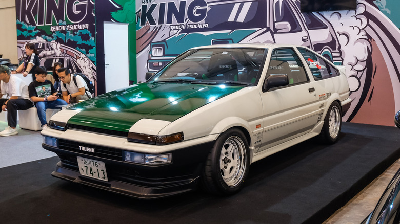 Front 3/4 view of white AE86 Toyota Corolla on display at car show.