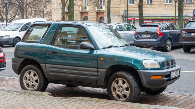 Side view of green first-generation Toyota RAV4 parked on city street.