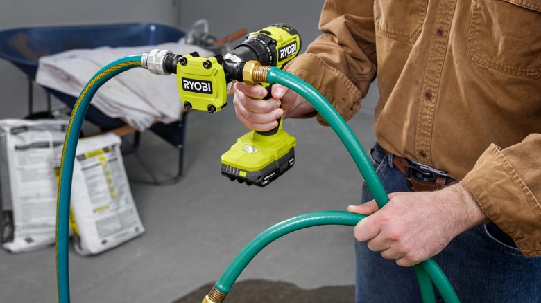A person holding a Ryobi drill with the 1/4" Hex Shank Drill Pump and hoses attached.