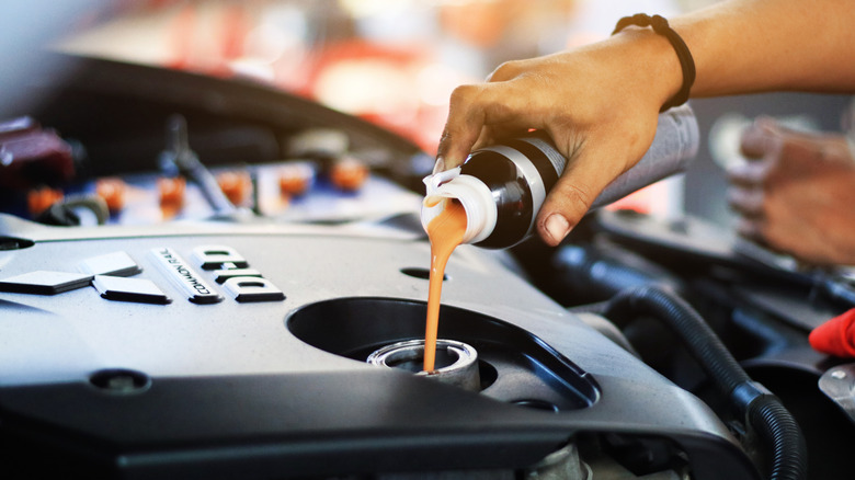 A hand pouring additives into a car engine