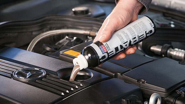 A person pouring a bottle of Cera Tec into their engine.