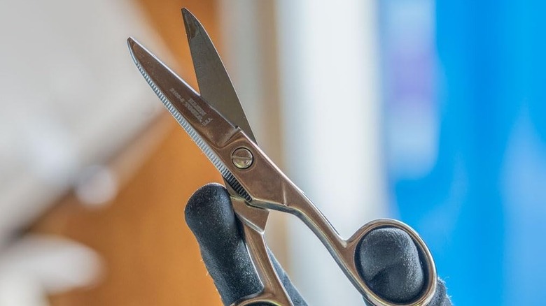 Klein Tools scissors held by gloved hands on a blurry background.