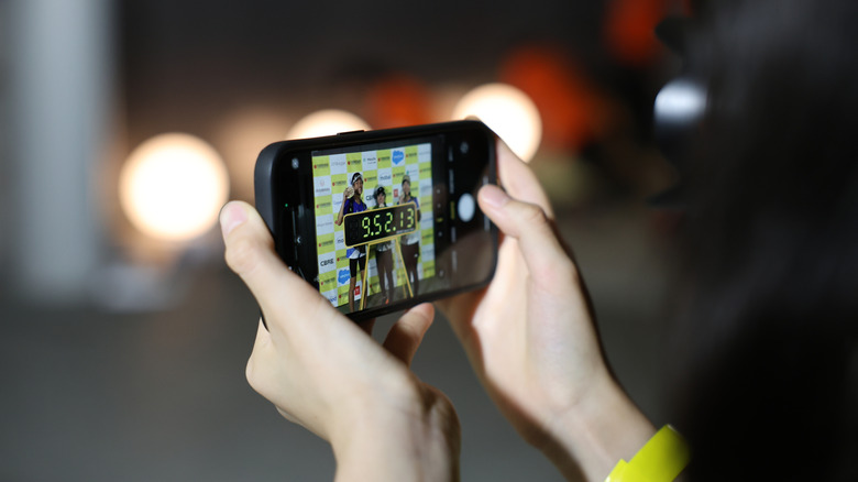 Hands holding an iPhone taking a photo of three marathon finishers