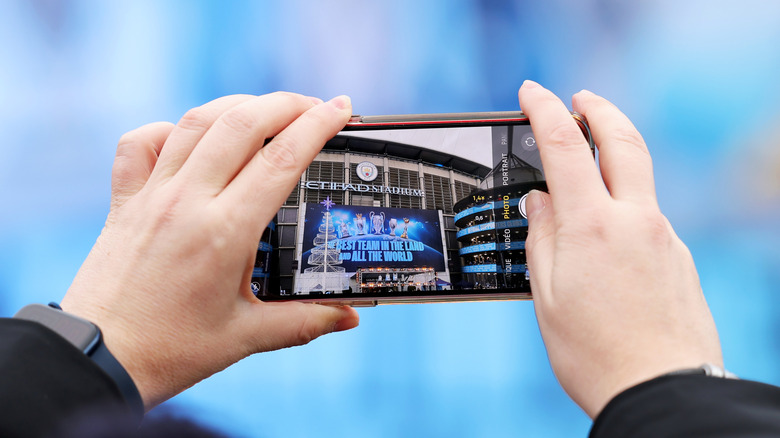 Hands holding an iPhone taking a photo of the Etihad Stadium