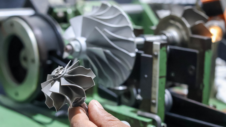 Technician inspecting turbocharger turbine wheel in workshop with other turbo components in background