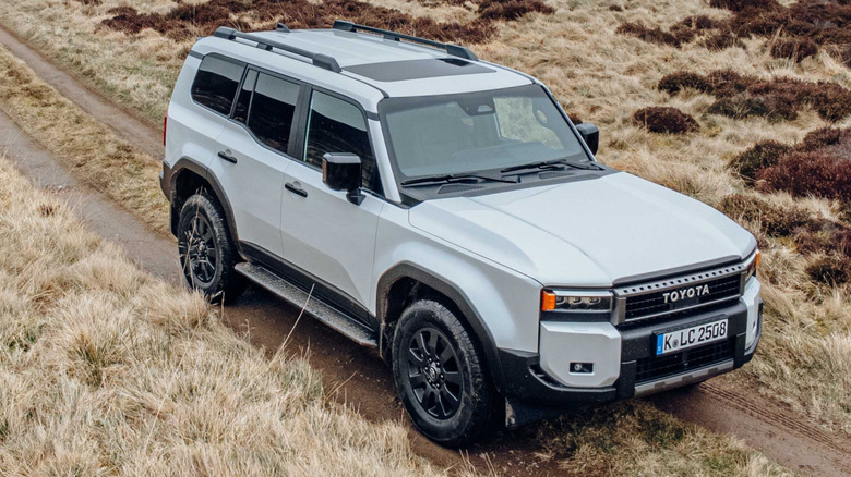 A white 2024 Toyota Land Cruiser seen from the left front, on rugged valley trail.